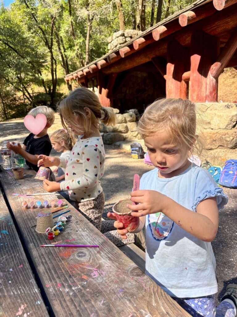 Children painting small flowerpots outdoors at Wilderness Cubs