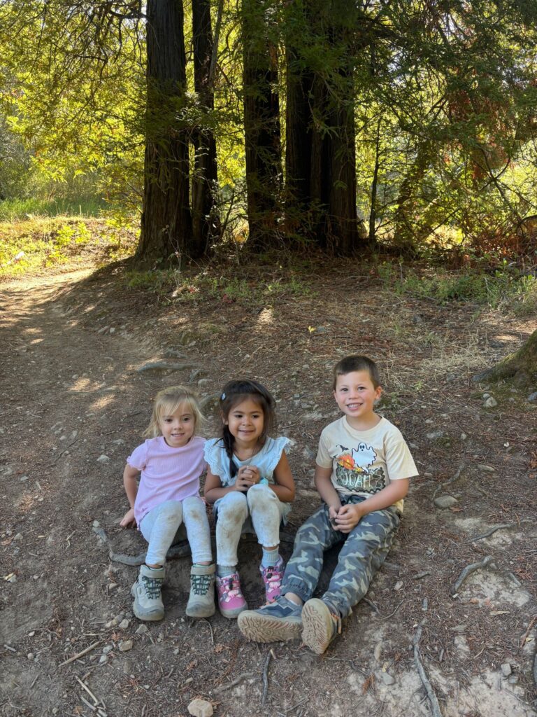 Three children sitting together in the woods during Wilderness Cubs
