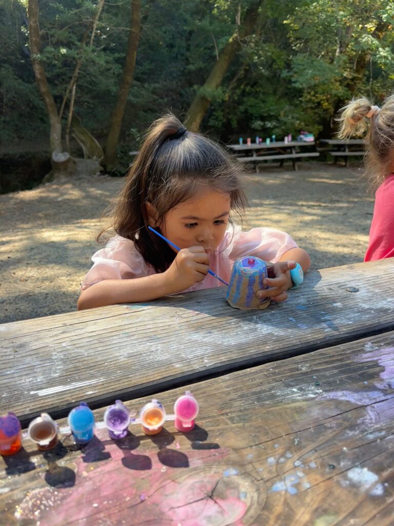 Child painting a small flowerpot outdoors at Wilderness Cubs